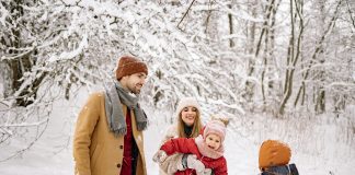 Winter Health Tips for Moms a family, husband, wife, two young children laughing and playing in the snow while trying to take picture; winter health tips for moms