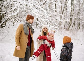 a family, husband, wife, two young children laughing and playing in the snow while trying to take picture; winter health tips for moms