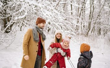 a family, husband, wife, two young children laughing and playing in the snow while trying to take picture; winter health tips for moms