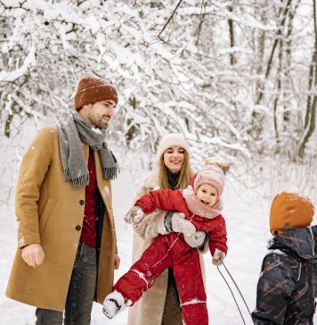 a family, husband, wife, two young children laughing and playing in the snow while trying to take picture; winter health tips for moms