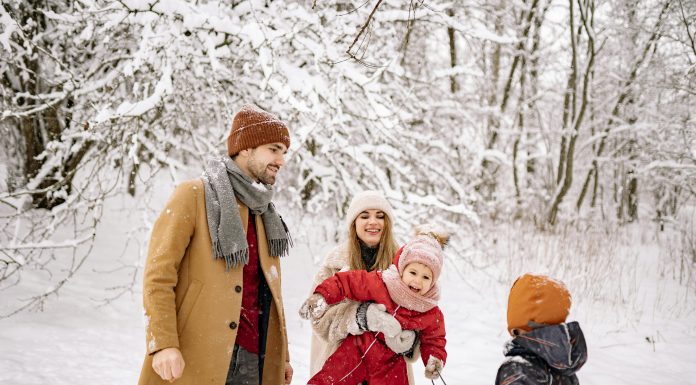 a family, husband, wife, two young children laughing and playing in the snow while trying to take picture; winter health tips for moms