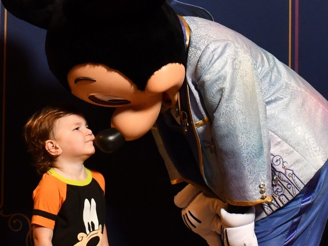 young child wearing a goofy shirt giving mickey mouse a kiss. ready for his first haricut at disney world