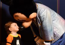 young child wearing a goofy shirt giving mickey mouse a kiss. ready for his first haricut at disney world