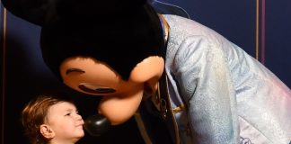 young child wearing a goofy shirt giving mickey mouse a kiss. ready for his first haricut at disney world