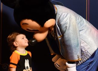 young child wearing a goofy shirt giving mickey mouse a kiss. ready for his first haricut at disney world