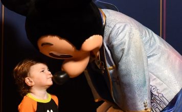 young child wearing a goofy shirt giving mickey mouse a kiss. ready for his first haricut at disney world