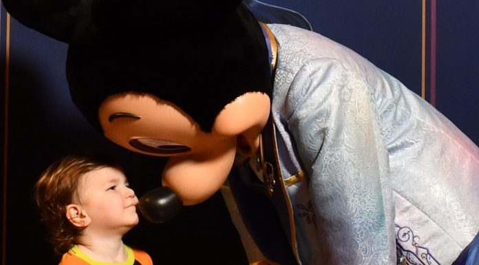 young child wearing a goofy shirt giving mickey mouse a kiss. ready for his first haricut at disney world