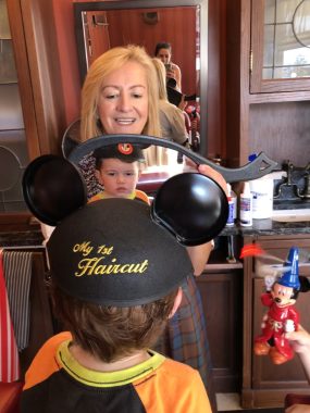 woman showing young boy wearing goofy shirt his first haircut at disney world