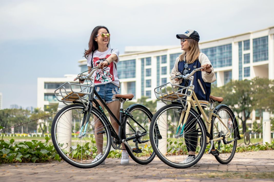 two men laughing on bicycles with a city scape in the back. Waiting for the latest travel trend
