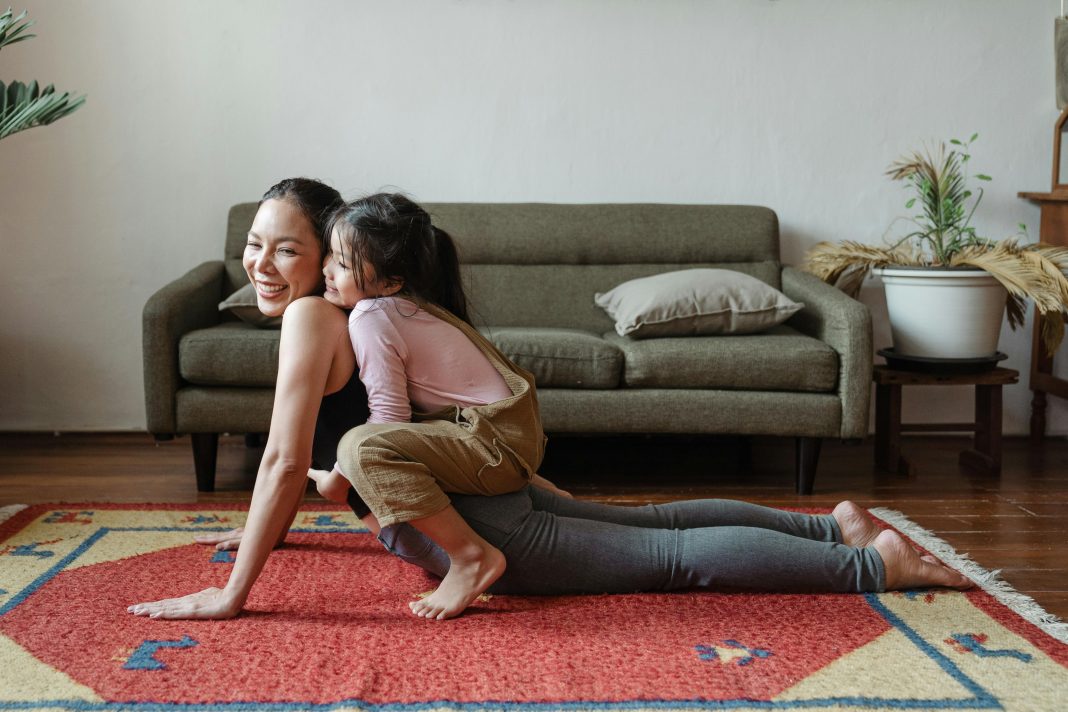 mom doing a yoga pose with child on top of her her. both are laughing, practicing good mental health habits.