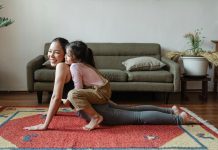 mom doing a yoga pose with child on top of her her. both are laughing, practicing good mental health habits.