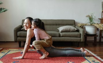 mom doing a yoga pose with child on top of her her. both are laughing, practicing good mental health habits.