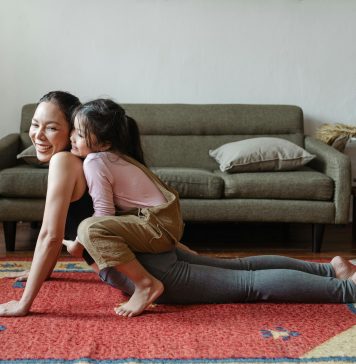 mom doing a yoga pose with child on top of her her. both are laughing, practicing good mental health habits.