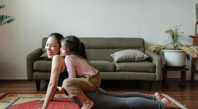 mom doing a yoga pose with child on top of her her. both are laughing, practicing good mental health habits.