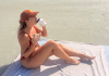 woman dribking coffee and eating a bagel on the beach in her swimwear worried about unexplained weight gain sporting a snackbitches hat