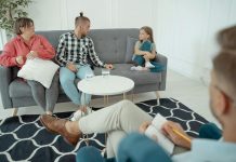 a therapist off to the side looking at a family, mom, dad, and young girl. body language suggests mild tension for family therapy