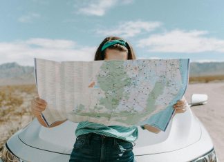 woman reading a map (can't see her face) resting against her car trying to avoid mistakes while traveling