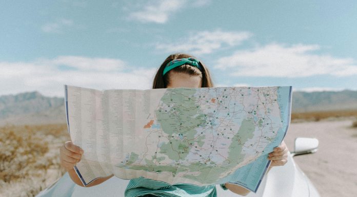 We Made Four Mistakes While Traveling — And How to Avoid Them woman reading a map (can't see her face) resting against her car trying to avoid mistakes while traveling