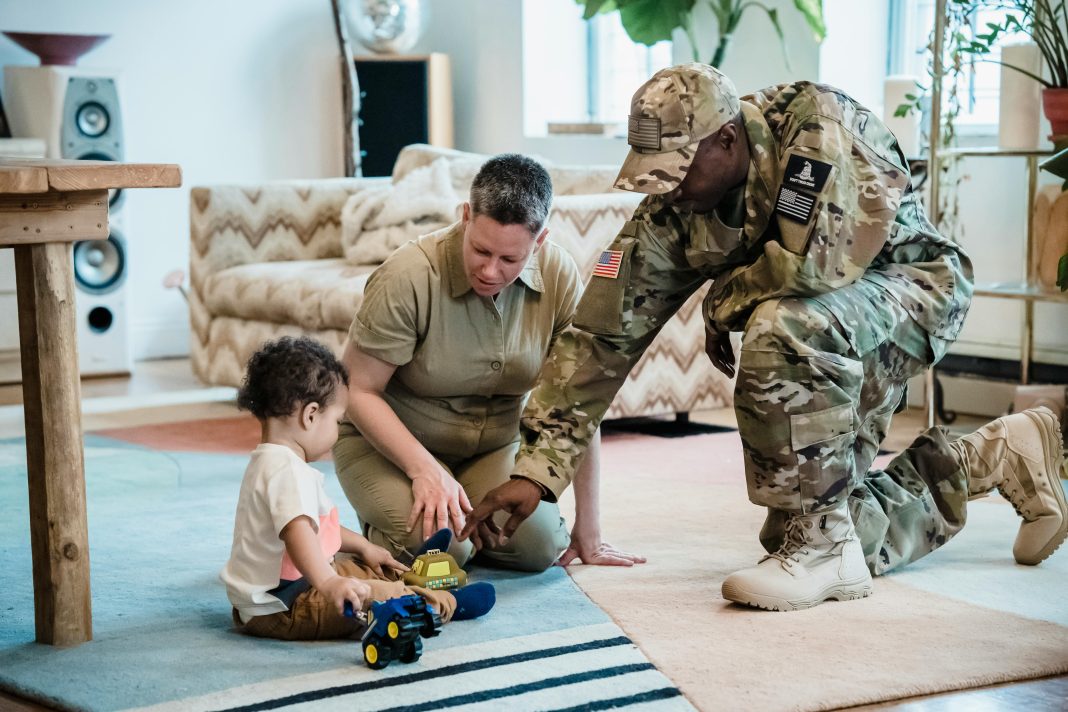 pexels-george-pak-7984308 A military mom and dad, both in uniform, help their young child play with toy trucks on a rug in their new living room—capturing a tender moment of family connection during a military moms PCS transition.