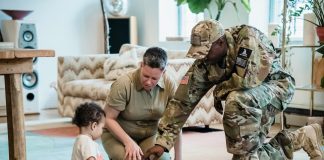 Military Moms PCS Guide: Building Home Wherever You Go A military mom and dad, both in uniform, help their young child play with toy trucks on a rug in their new living room—capturing a tender moment of family connection during a military moms PCS transition.
