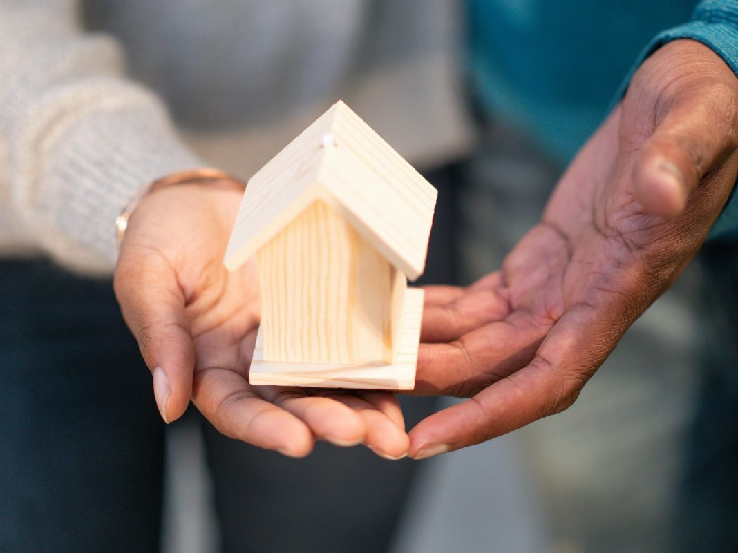 a couple holding a wooden house either because they're buying or selling a home