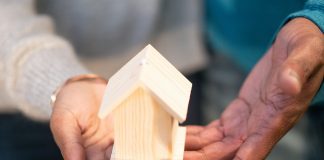 What Every Mom Should Know Before Buying or Selling a Home a couple holding a wooden house either because they're buying or selling a home