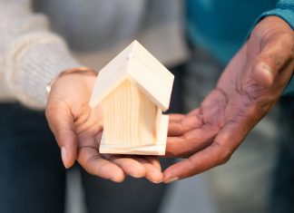 a couple holding a wooden house either because they're buying or selling a home