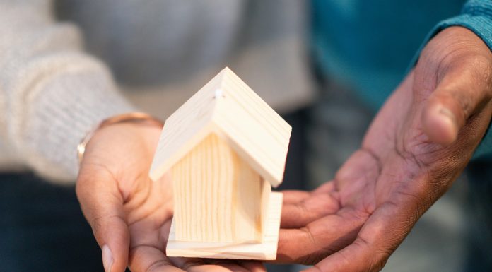What Every Mom Should Know Before Buying or Selling a Home a couple holding a wooden house either because they're buying or selling a home