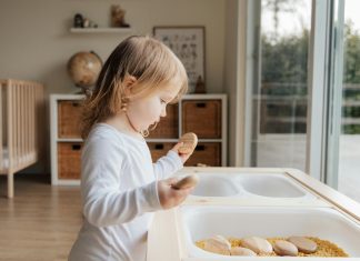 child in sensory play with smooth rocks and dry macaroni