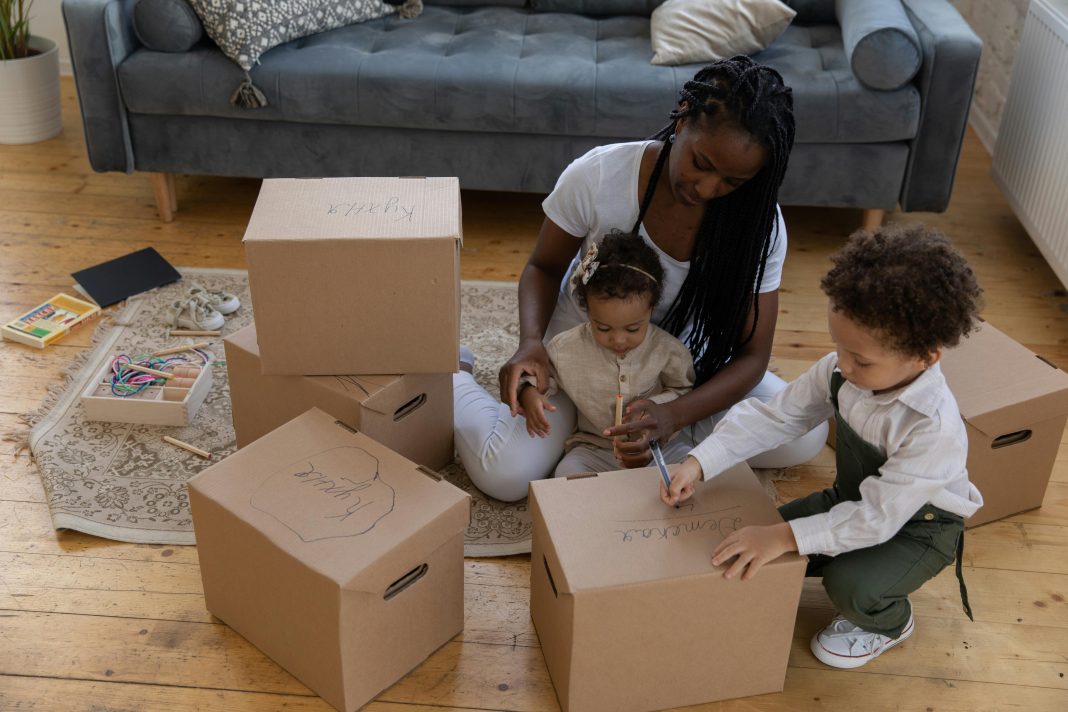 Mother sitting on the floor with her two young children, labeling cardboard boxes together for indoor activities in orlando.