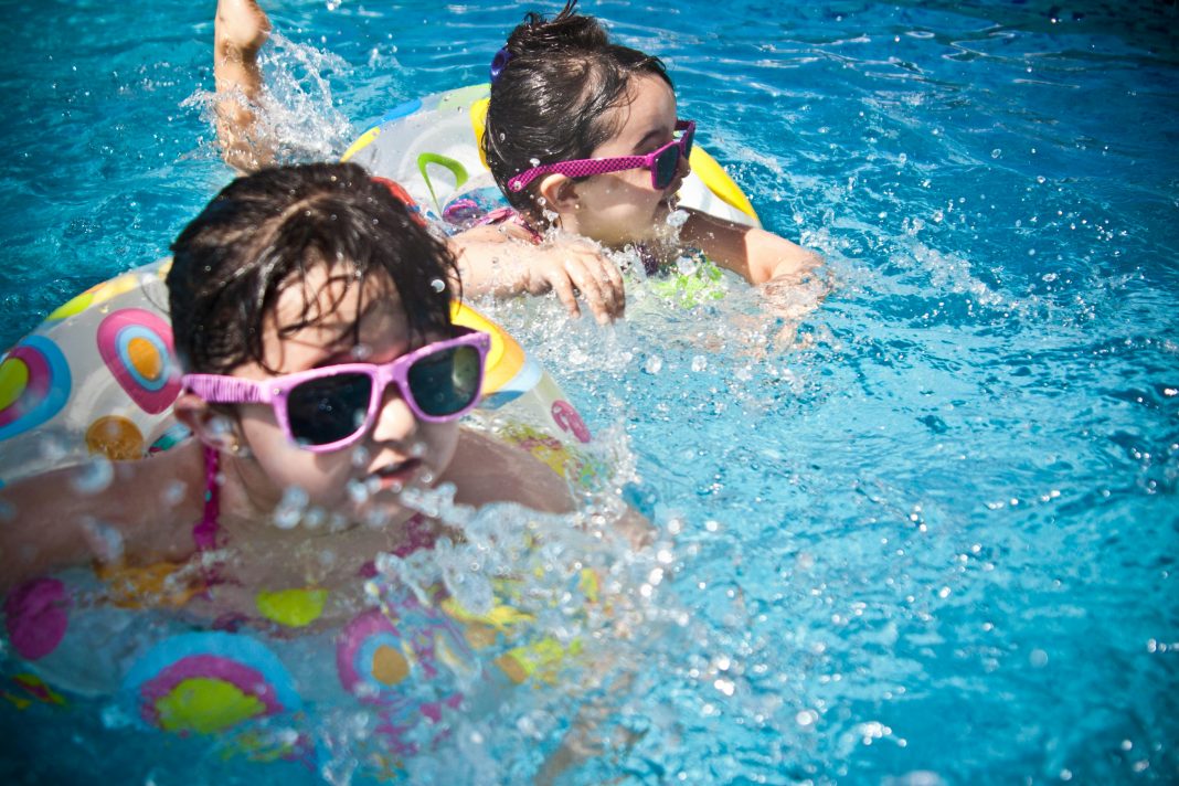 Two young children wearing sunglasses and colorful swimsuits play in a pool, a fun way of surviving summer in Orlando and staying cool during the heat.