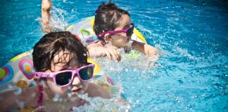 Two young children wearing sunglasses and colorful swimsuits play in a pool, a fun way of surviving summer in Orlando and staying cool during the heat.