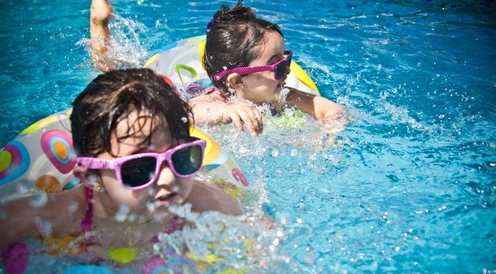Surviving Summer in Orlando: A Local Mom’s Guide to Beat the Orlando Summer Heat With Kids Two young children wearing sunglasses and colorful swimsuits play in a pool, a fun way of surviving summer in Orlando and staying cool during the heat.