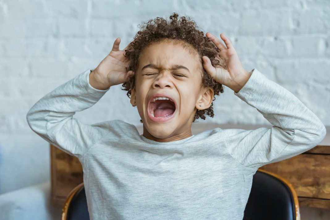 pexels-keira-burton-6624327 Young child mid-toddler tantrum with eyes closed, mouth open yelling, and hands raised to head in frustration.