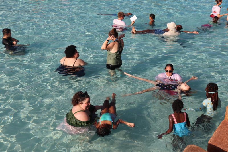 Instructors guide children through floating exercises during the world’s largest swimming lesson, with families standing waist-deep in the clear lagoon.