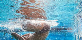 Swimmer performing an underwater flip turn in a pool, highlighting athletic skill and promoting water safety awareness.