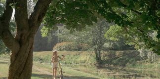 Young girl walking her yellow bike along a leafy pond path on a sunny day, illustrating screen-free summer activities for kids.