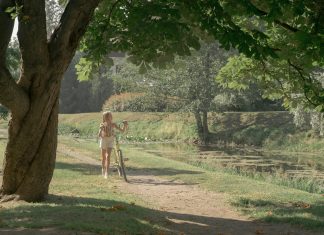 Young girl walking her yellow bike along a leafy pond path on a sunny day, illustrating screen-free summer activities for kids.