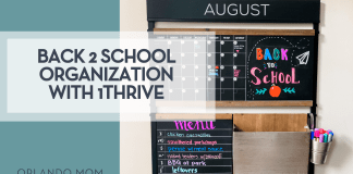 Back-to-School Organization with 1Thrive wall command center showing an August calendar, colorful “Back to School” chalk art, weekly menu board, mail pocket, and cup of markers—all mounted on a sleek black frame for streamlined family scheduling.