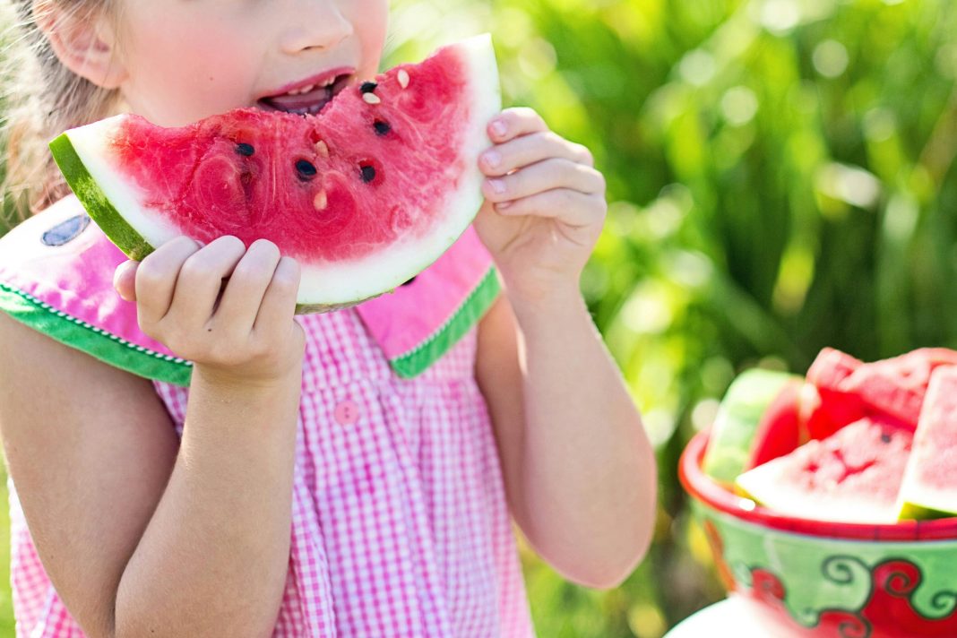 girl eating sliced watermelon fruit beside table during summer break