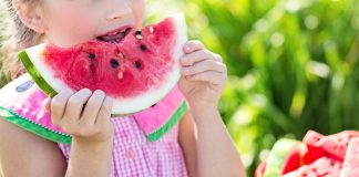 Summer Break Help: The Child-Free Auntie’s Guide to Showing Up girl eating sliced watermelon fruit beside table during summer break
