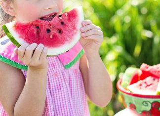 Summer Break Help: The Child-Free Auntie’s Guide to Showing Up girl eating sliced watermelon fruit beside table during summer break