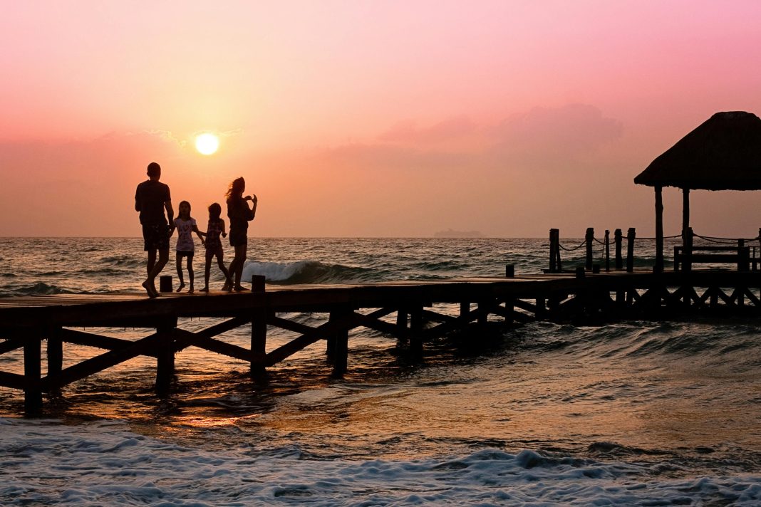 Family standing on a oceanside dock at sunrise, illustrating Summer Travel Tips for Families with Autistic Children.