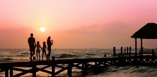 Family standing on a oceanside dock at sunrise, illustrating Summer Travel Tips for Families with Autistic Children.