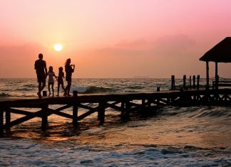 Family standing on a oceanside dock at sunrise, illustrating Summer Travel Tips for Families with Autistic Children.