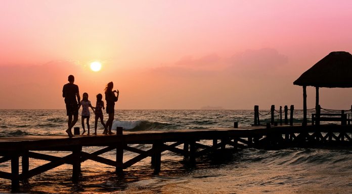 10 Summer Travel Tips for Families with Autistic Children Family standing on a oceanside dock at sunrise, illustrating Summer Travel Tips for Families with Autistic Children.
