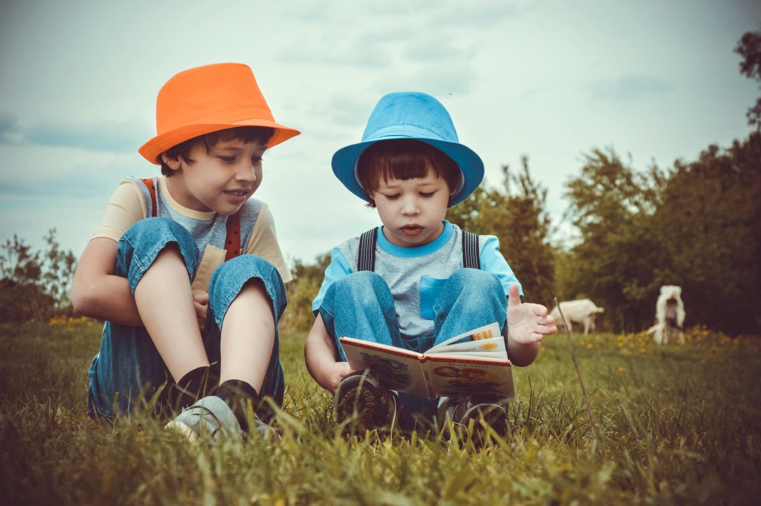 Early-elementary children reading colorful books together on a sunny grass field—an engaging outdoor activity to help prevent summer slide.