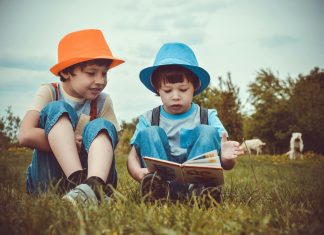 Early-elementary children reading colorful books together on a sunny grass field—an engaging outdoor activity to help prevent summer slide.