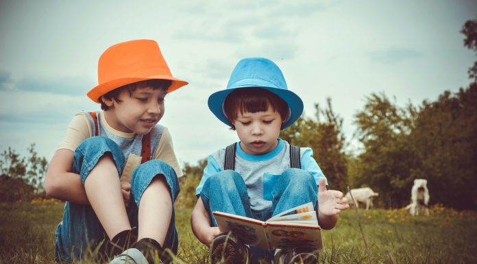 6 Ways to Prevent Summer Slide for Early Elementary Early-elementary children reading colorful books together on a sunny grass field—an engaging outdoor activity to help prevent summer slide.