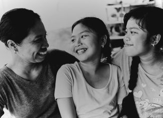 Back-to-School Health: Everyday Habits to Keep Mom Energized and Injury-Free Black and white image of a smiling mom sitting on the floor with her children in a cozy living room, showing a moment of connection and balance, reflecting Mom Back to School health.